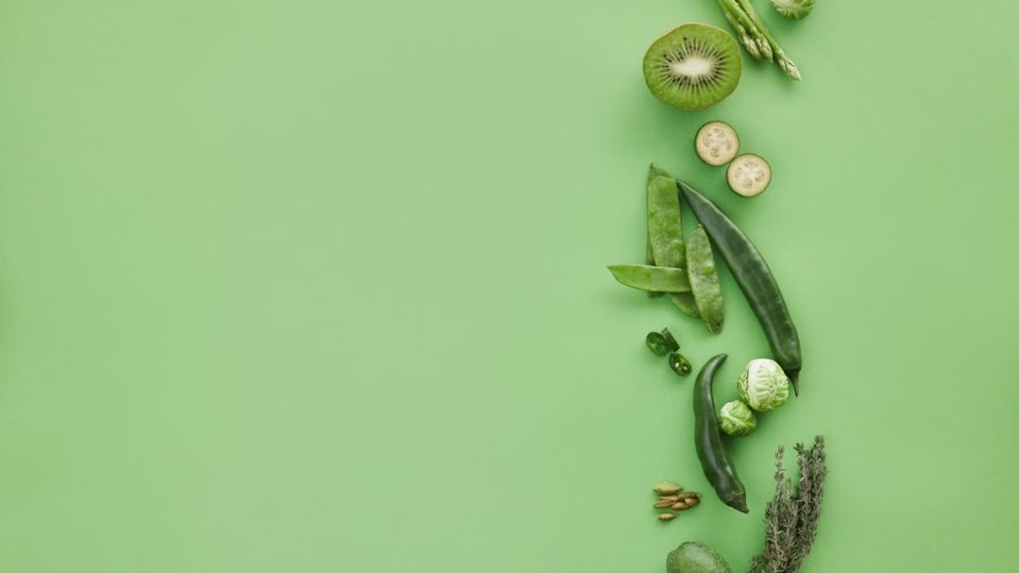 Colorful arrangement of fresh green fruits and vegetables on a green background, top view, with copy space.