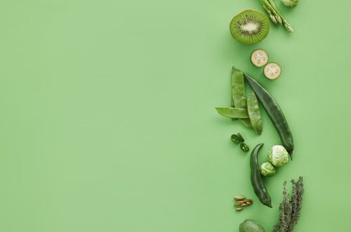 Colorful arrangement of fresh green fruits and vegetables on a green background, top view, with copy space.